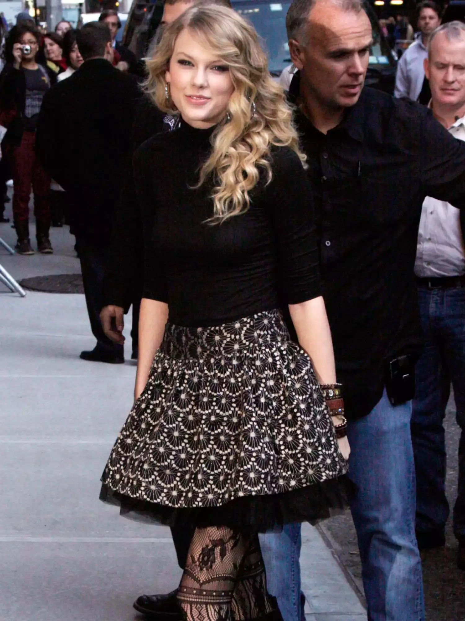 Taylor Swift wearing voluminous patterned skirt, black top, and black lace floral tights